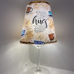 Handgefertigte Lichtinsel mit bunt kolorierten Tassen, Spruch „Tea is a hug in a cup“ und Teefleckstruktur in warmen Brauntönen, inklusive LED-Lichterkette