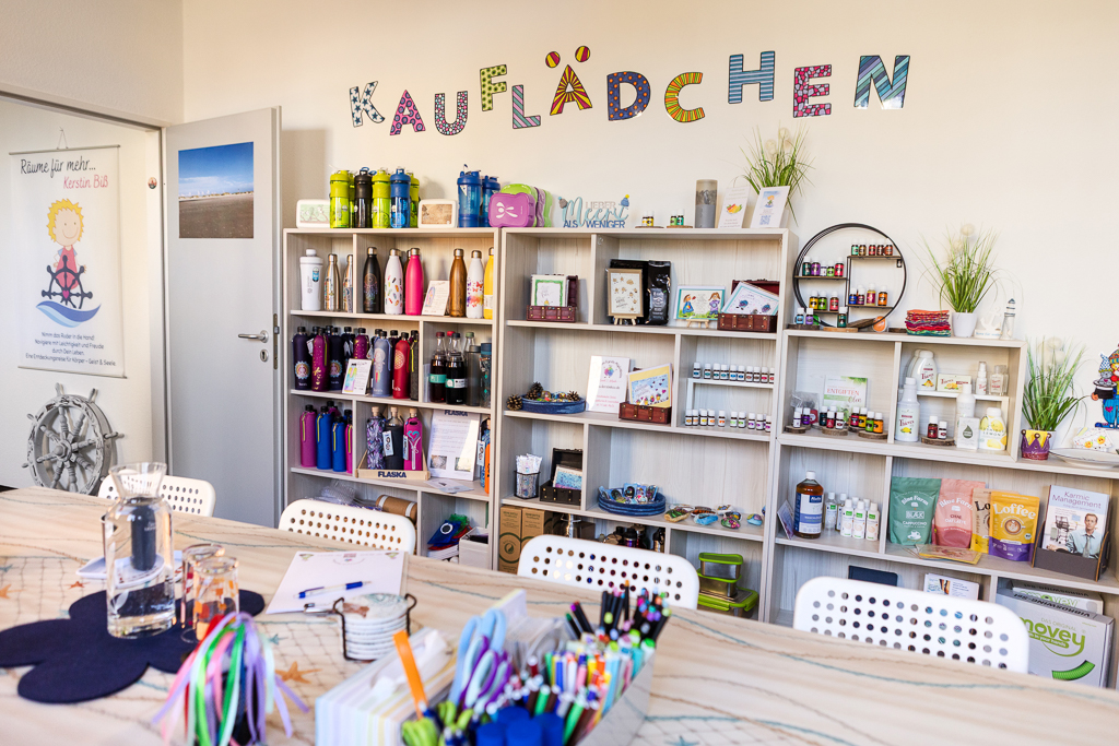 Regale im Kauflädchen von Räume für mehr mit Trinkflaschen, ätherischen Ölen, Naturkosmetik, Büchern und kreativen Accessoires; im Vordergrund ein Basteltisch mit Stiften und Materialien