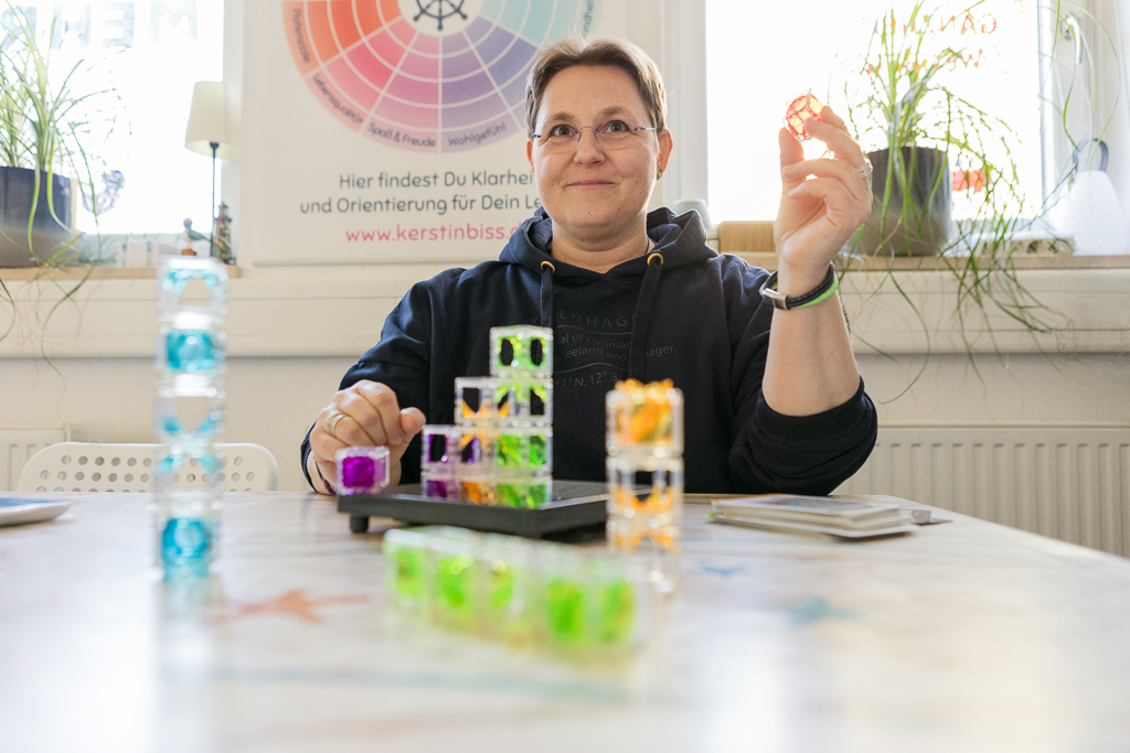 Kerstin Biß sitzt an einem Tisch mit bunten Strukturwürfeln und lächelt – kreative Coachingarbeit in ihrem Studio in Nürnberg